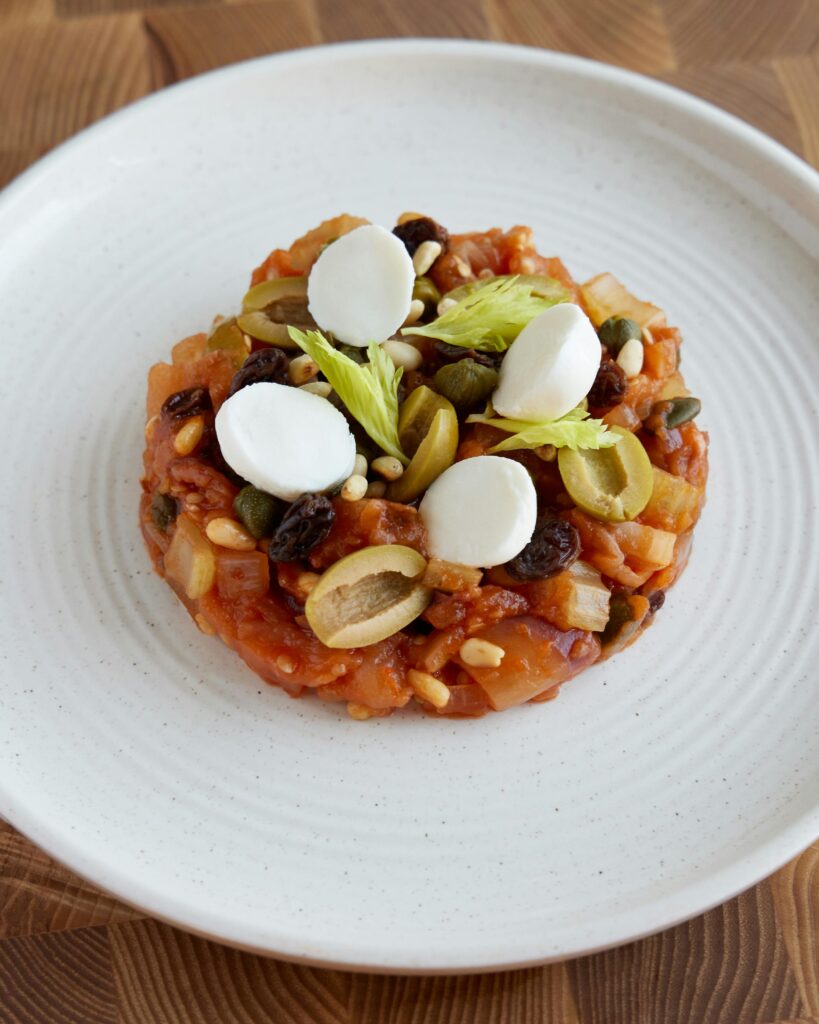 Delicious Sicilian caponata with olives and mozzarella on a ceramic plate.