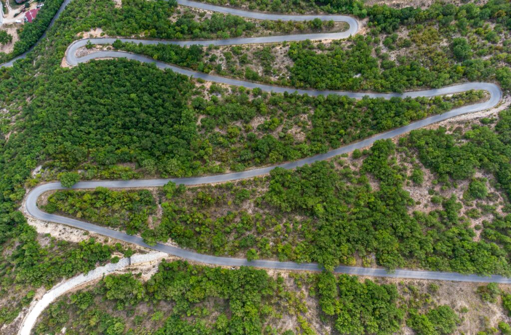 Aerial shot of a zigzag road cutting through lush green countryside landscape.